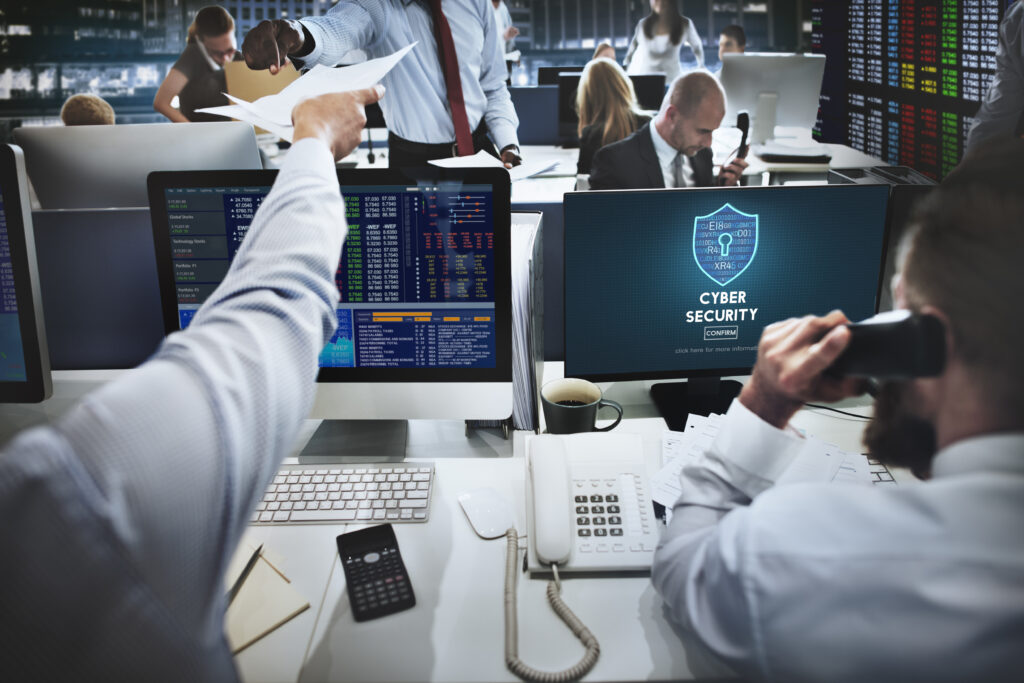 Mitarbeiter in Großraumbüro mit Monitoren und Cyber-Security-Display