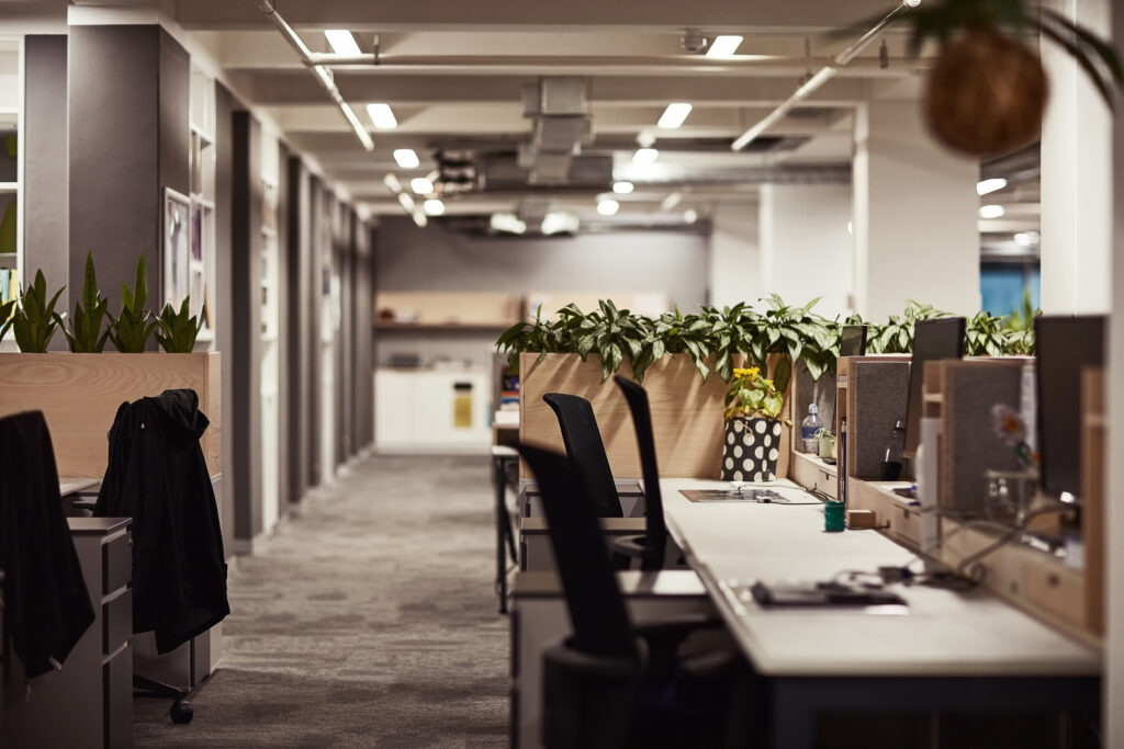 Stilvolles, leeres Büro mit Schreibtischen, Monitoren, Pflanzen und LED-Beleuchtung