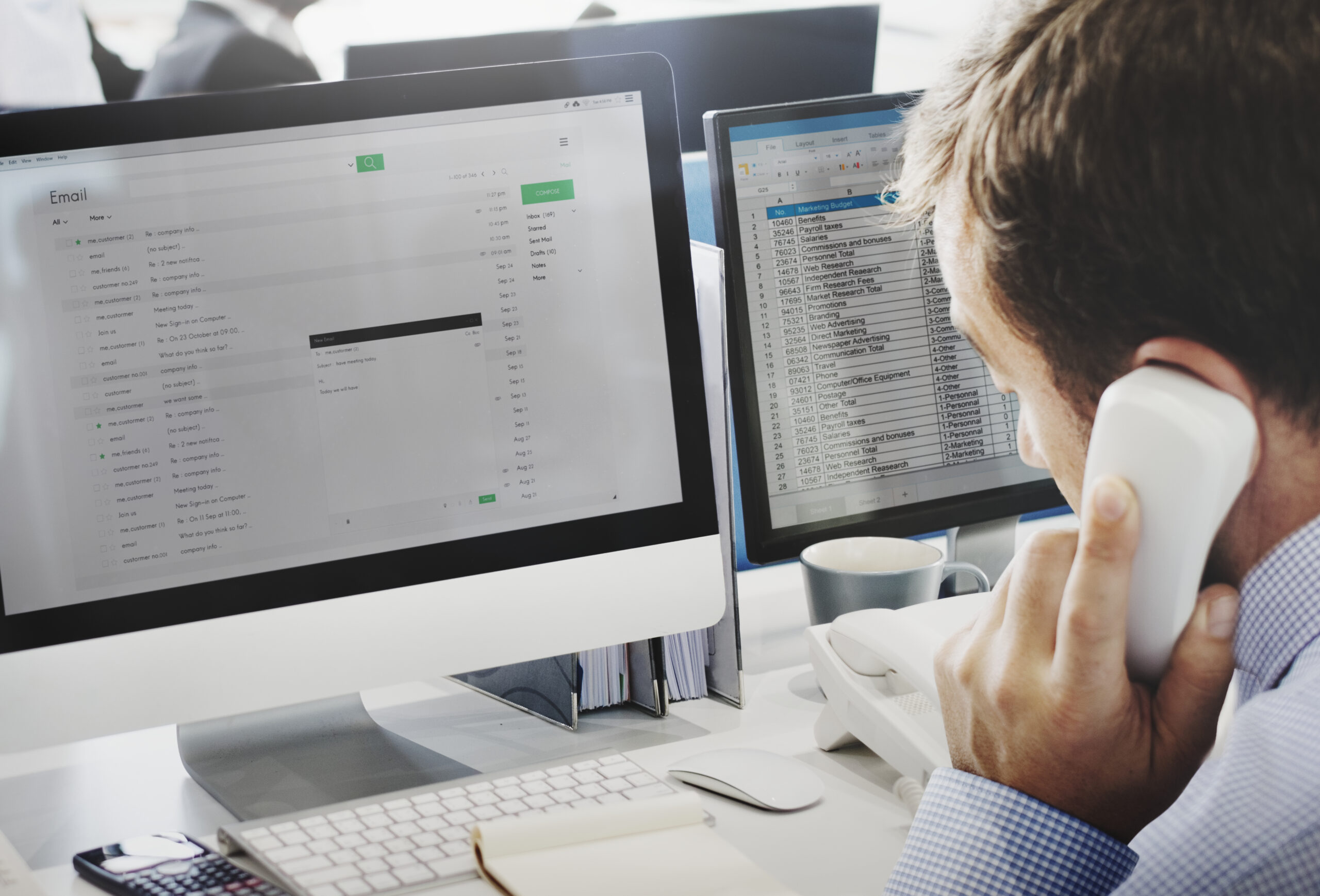 Geschäftsmann telefoniert vor zwei Monitoren mit E-Mail- und Tabellensoftware