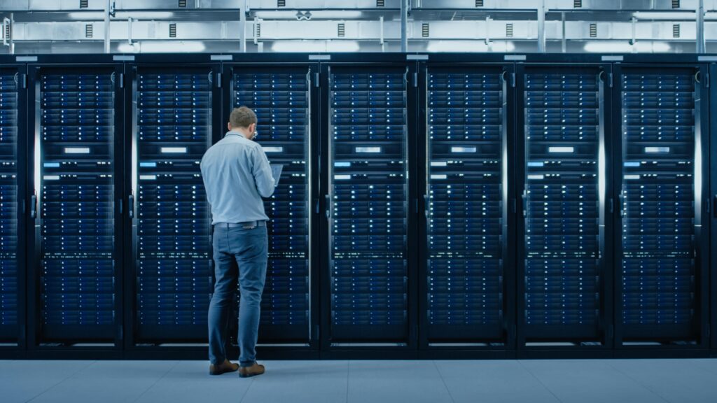 Nachdenklicher IT-Profi blickt auf Serverracks in einem hellen Serverraum mit laufenden Systemen