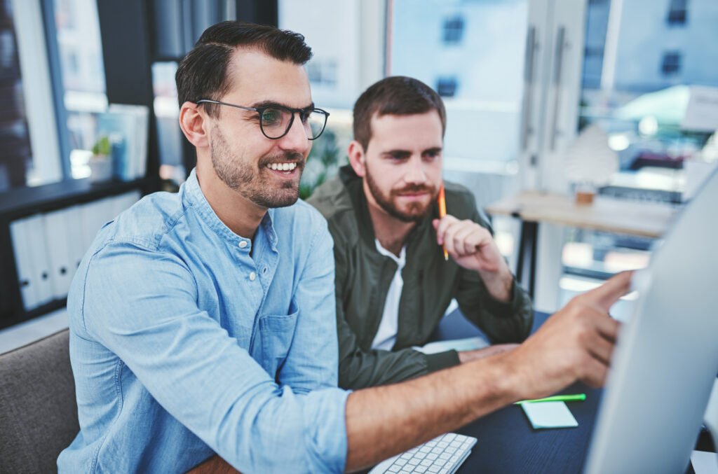 Zwei Kollegen besprechen IT-Lösungen vor einem Monitor im Büro